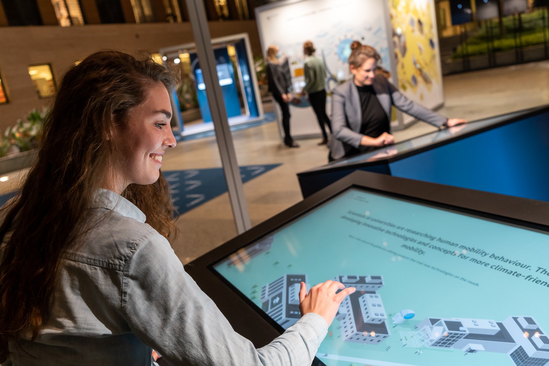 Eine Besucherin der Wanderausstellung sitzt an einem Bildschirm der Station „Mobilität“ und sieht sich die Inhalte der Wissenschaft-Perspektive an. 
